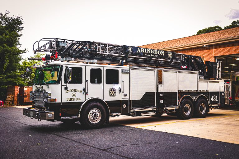 A black and white Abingdon fire truck with an extended ladder is parked outside a brick fire station on a paved driveway. The truck is marked "431" and "Abingdon Fire Co." in white letters.