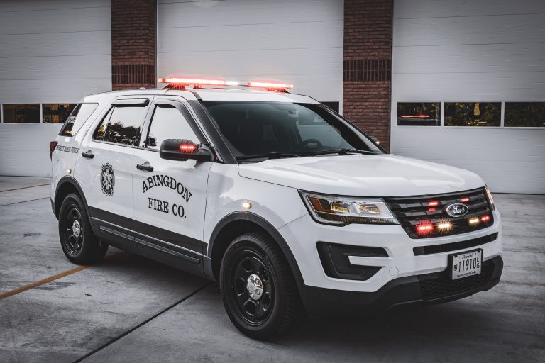 A white Abingdon Fire Co. SUV with red emergency lights flashing is parked in front of garage doors at a fire station.
