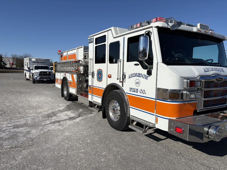 A white and orange fire truck with "Abingdon Fire Co." on the side is parked on a sunny day, followed by an ambulance in a mostly empty lot with clear blue sky above.