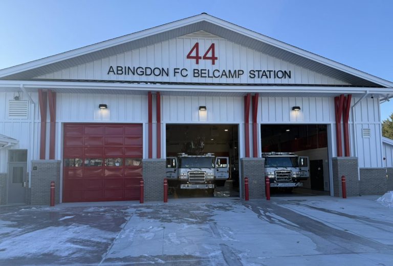 A fire station labeled "44 ABINGDON FC BELCAMP STATION" with three garage doors, two of which are open showing fire trucks inside. The station has a white exterior with red accents.