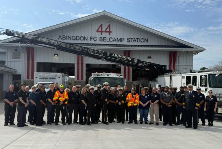 A large group of firefighters and emergency personnel stand in front of the Abingdon FC Belcamp Station 44, with fire trucks and equipment visible behind them on a sunny day.